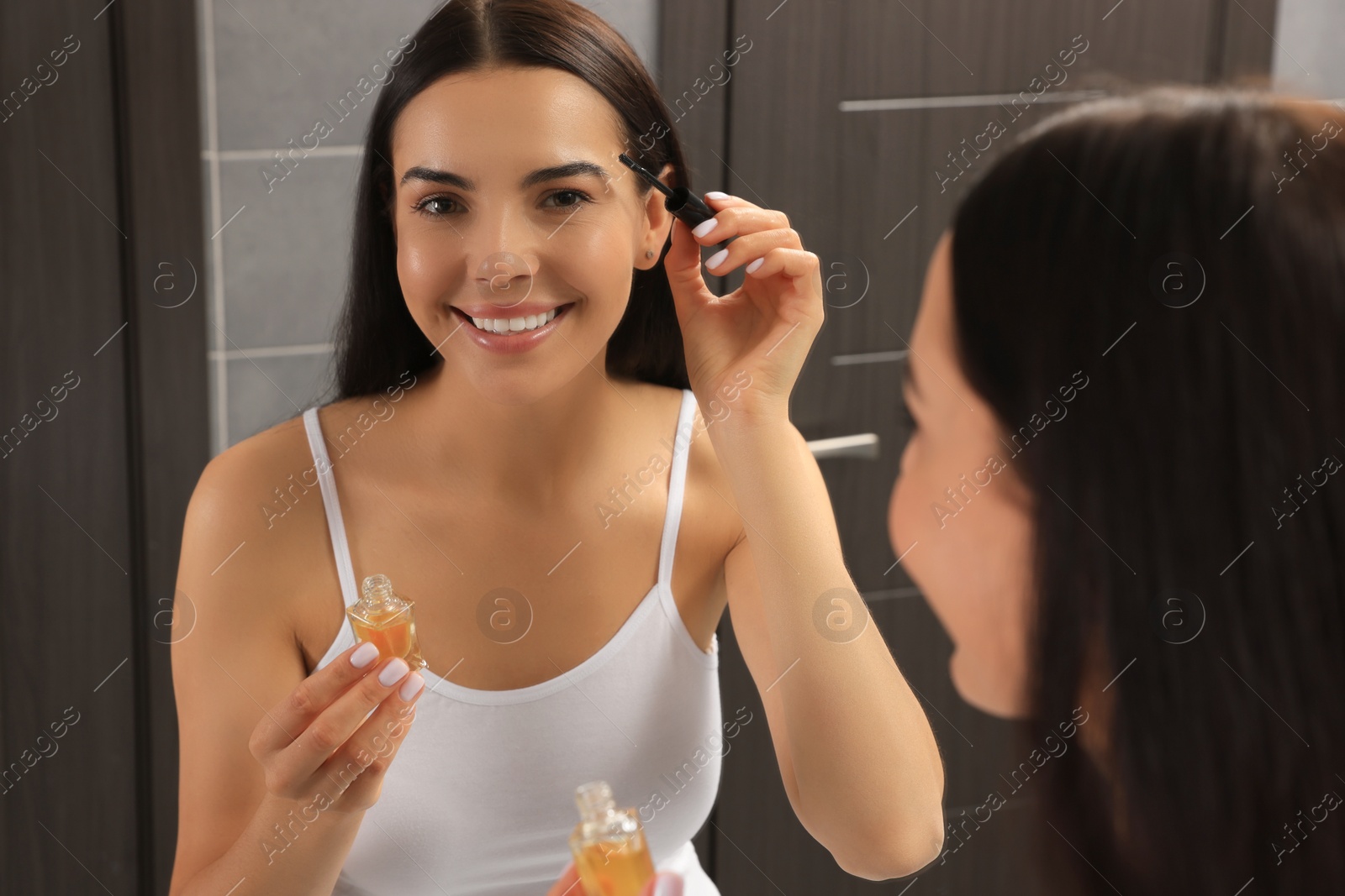 Photo of Young woman with eyelash oil in bathroom