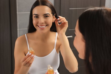 Photo of Young woman with eyelash oil in bathroom