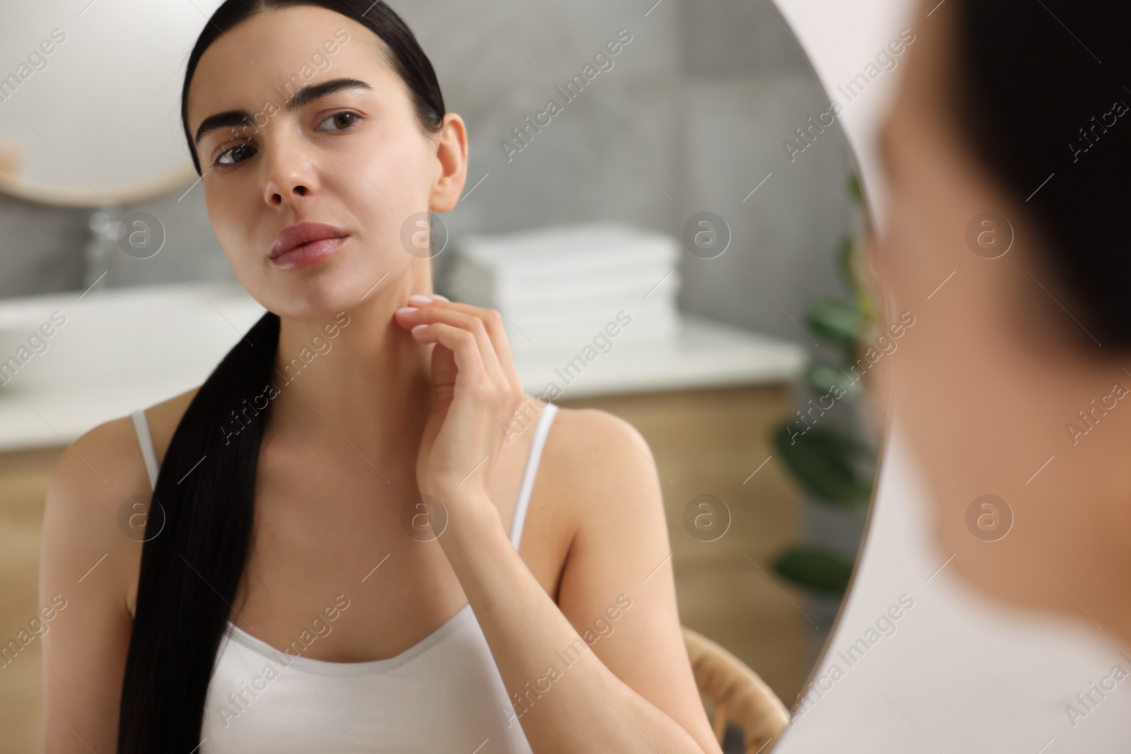 Photo of Woman with dry skin looking at mirror in bathroom