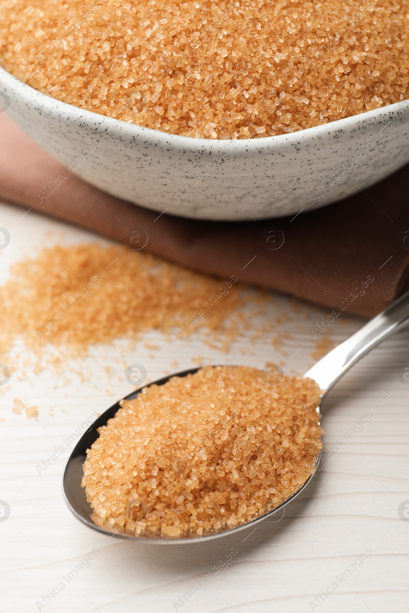 Photo of Spoon and bowl with brown sugar on white wooden table, closeup