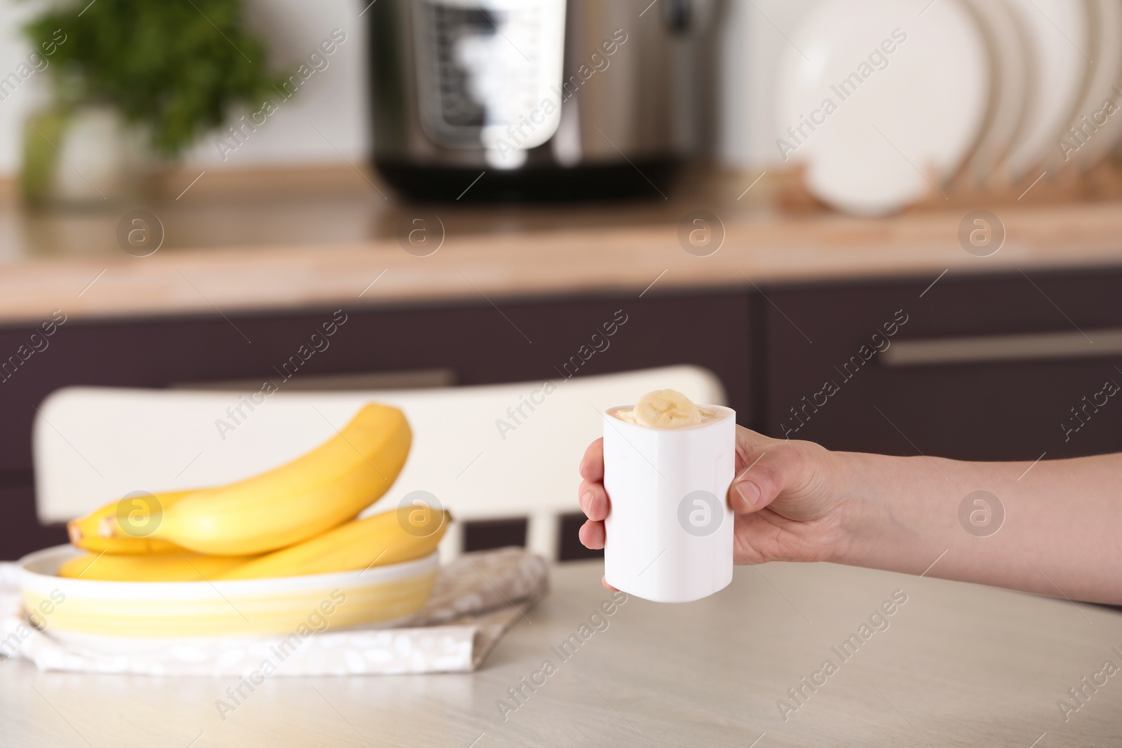 Photo of Woman holding container with delicious fresh yogurt made in modern multi cooker over table, closeup. Space for text