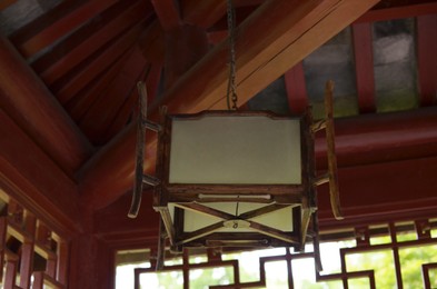 Photo of Decorative asian wooden lamp hanging in room. Interior design