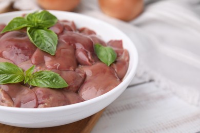 Bowl with raw chicken liver and basil on white wooden table, closeup. Space for text