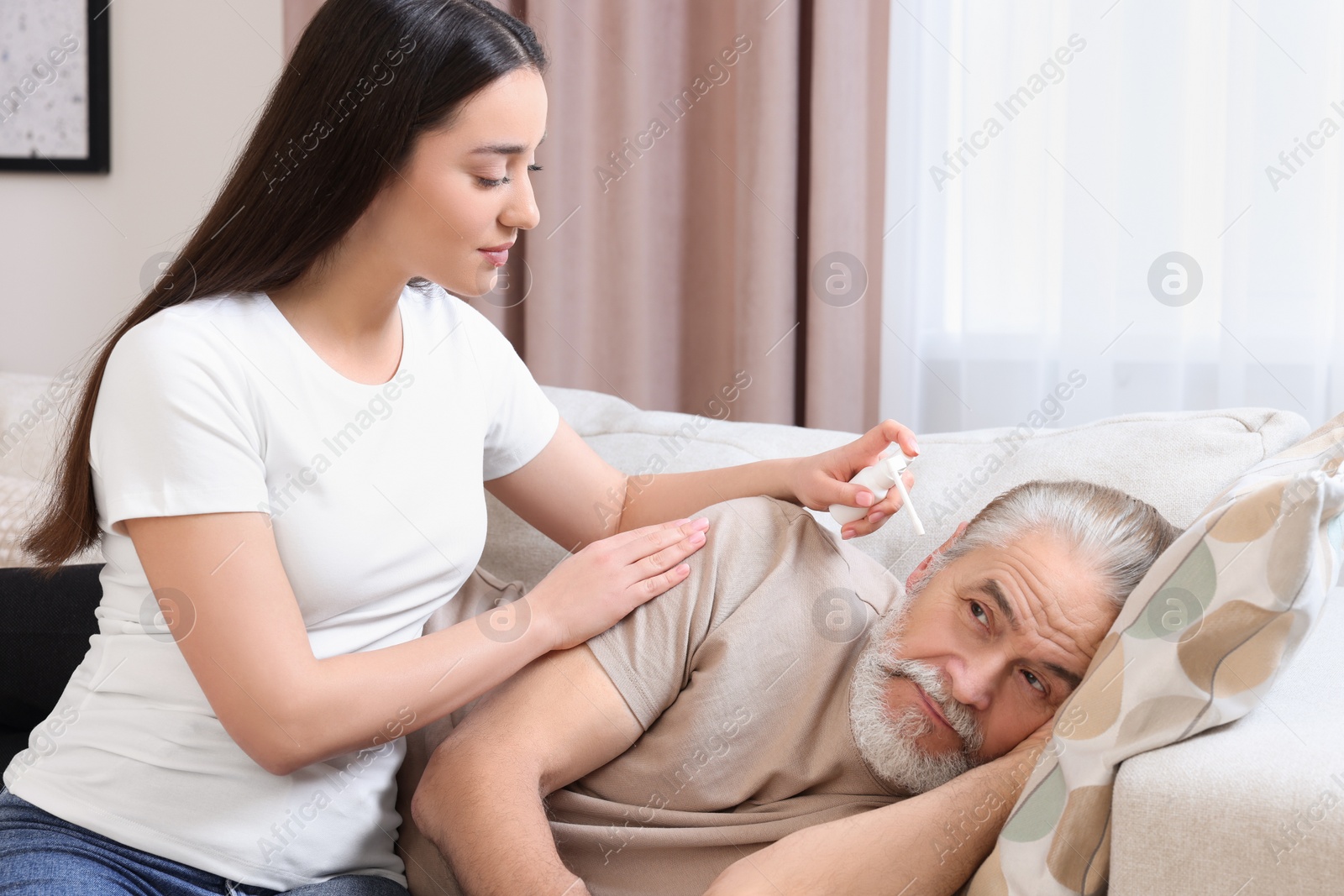 Photo of Young woman spraying medication into man's ear at home