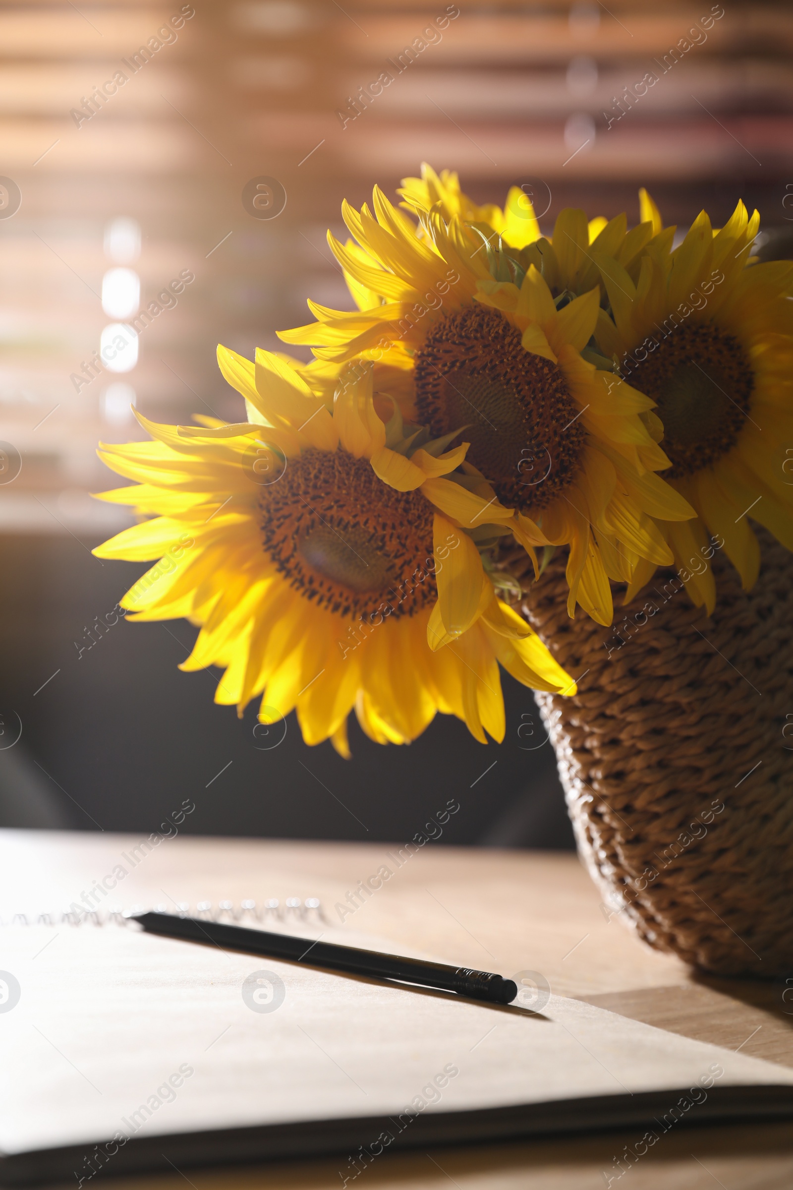 Photo of Bouquet of beautiful sunflowers, notebook and pencil  on table indoors, closeup