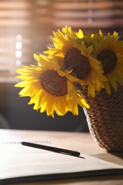 Bouquet of beautiful sunflowers, notebook and pencil  on table indoors, closeup