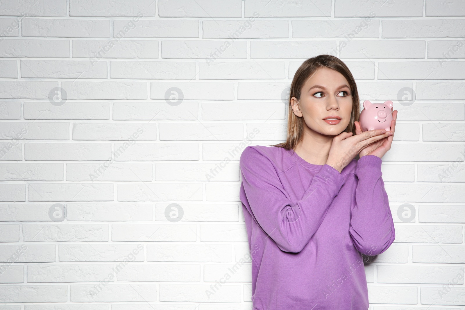 Photo of Young woman with piggy bank on brick wall background. Space for text