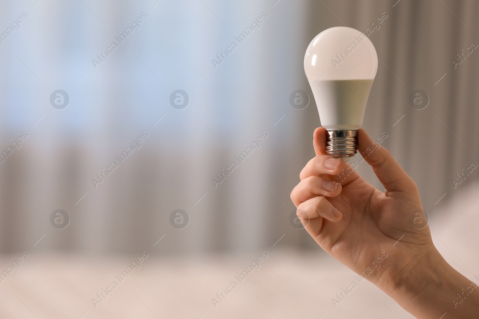 Photo of Woman holding fluorescent light bulb on blurred background, closeup with space for text. Saving energy concept