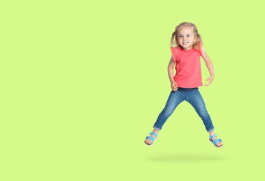 Cute girl jumping on light green background, space for text