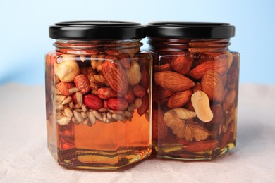 Photo of Jars with different nuts and honey on beige background, closeup