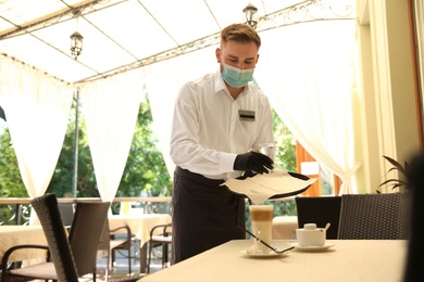 Photo of Waiter serving beverages in restaurant. Catering during coronavirus quarantine