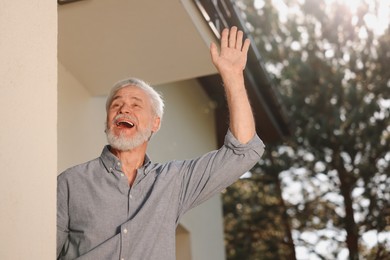 Photo of Neighbor greeting. Happy senior man waving near house outdoors, low angle view