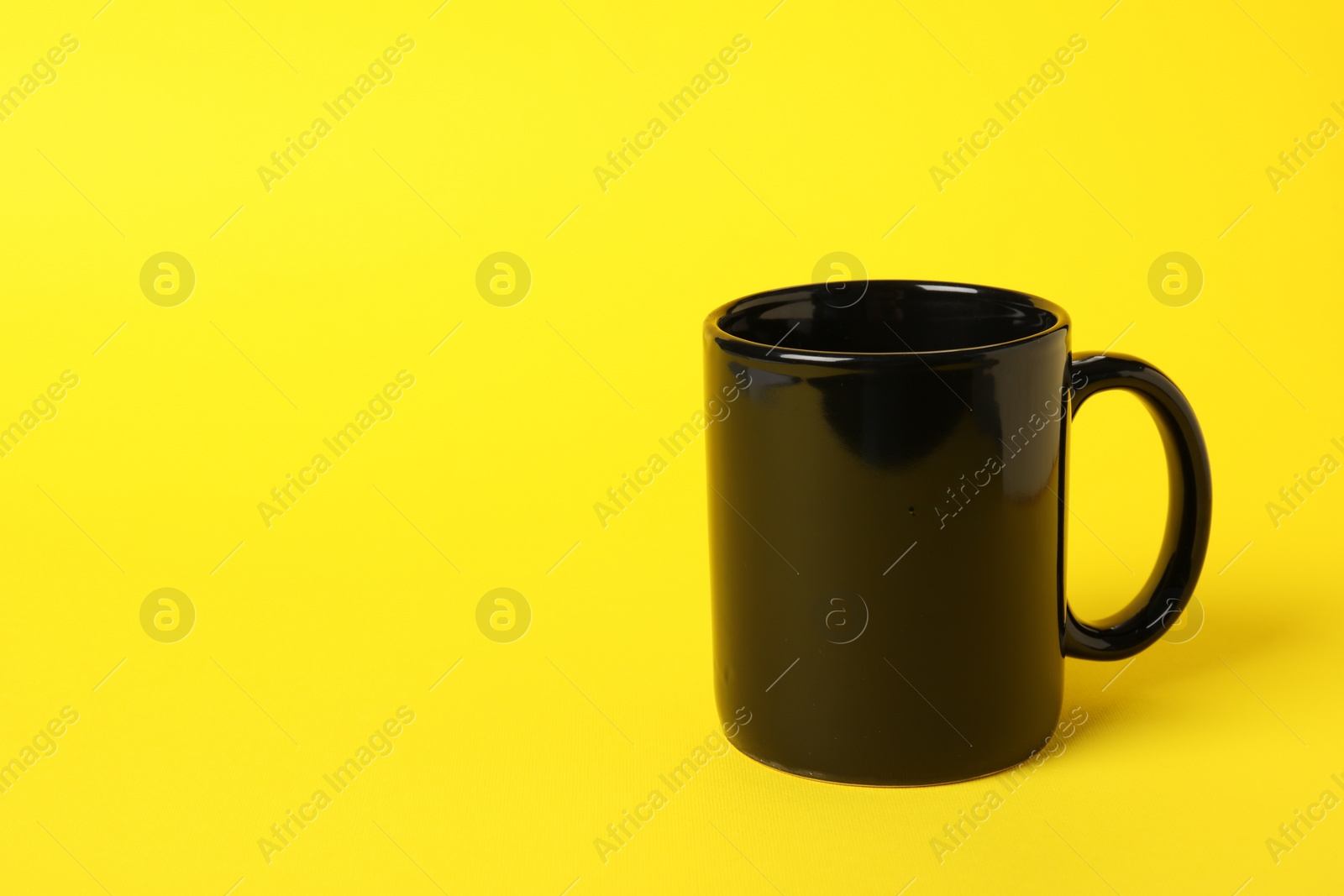 Photo of One black ceramic mug on yellow background, space for text