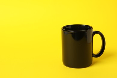 Photo of One black ceramic mug on yellow background, space for text