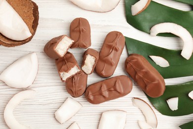 Photo of Delicious milk chocolate candy bars with coconut filling on white wooden table, flat lay