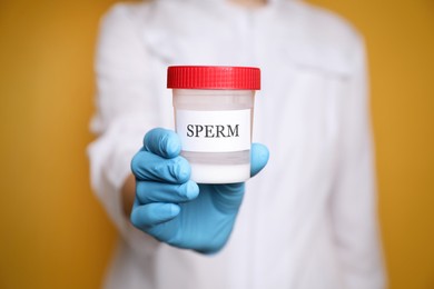 Scientist holding container with sperm on yellow background, closeup