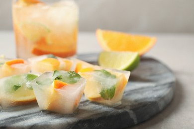 Photo of Ice cubes with orange and mint on light grey table, closeup