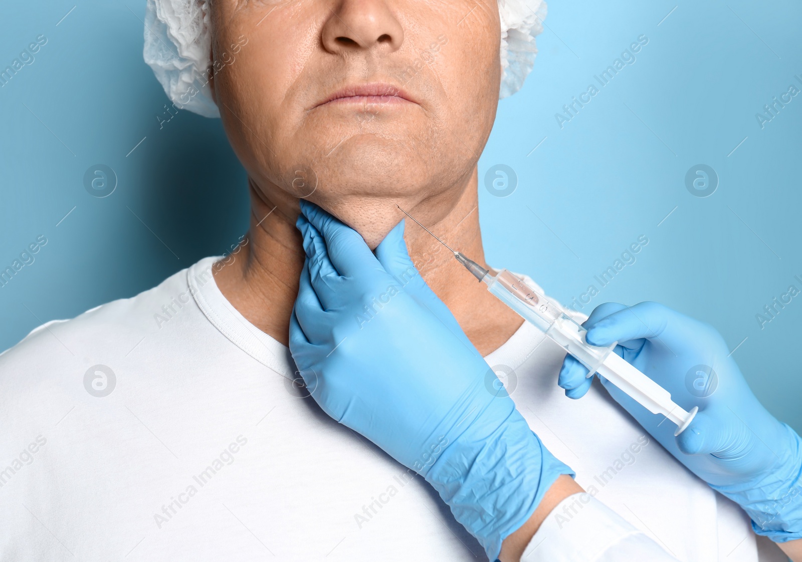 Photo of Mature man with double chin receiving injection on blue background, closeup