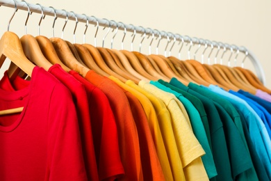 Photo of Rack with bright clothes on light background. Rainbow colors