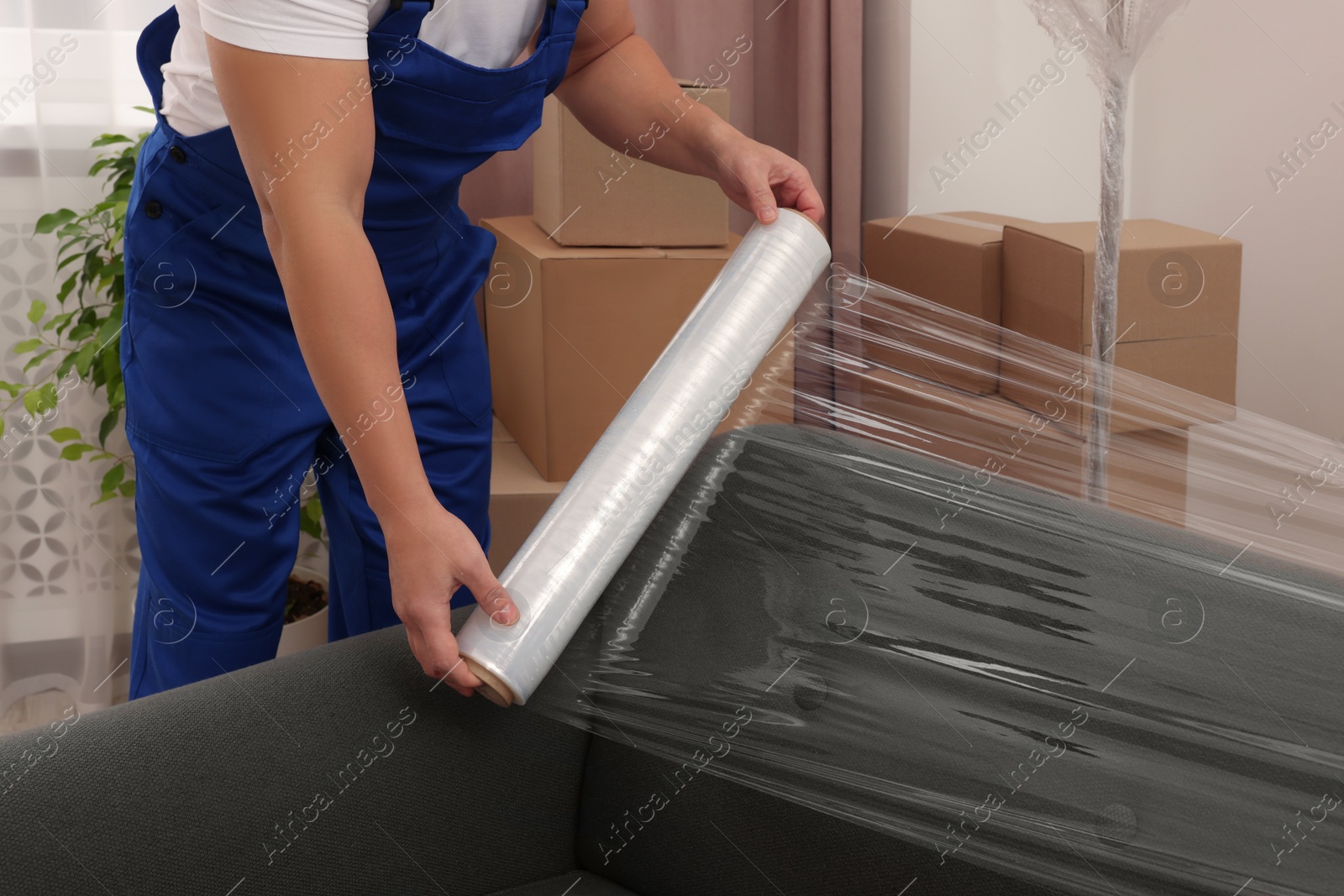 Photo of Worker wrapping sofa in stretch film indoors, closeup