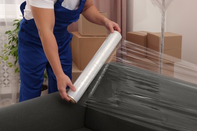 Worker wrapping sofa in stretch film indoors, closeup