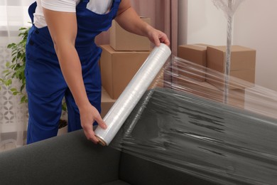 Photo of Worker wrapping sofa in stretch film indoors, closeup