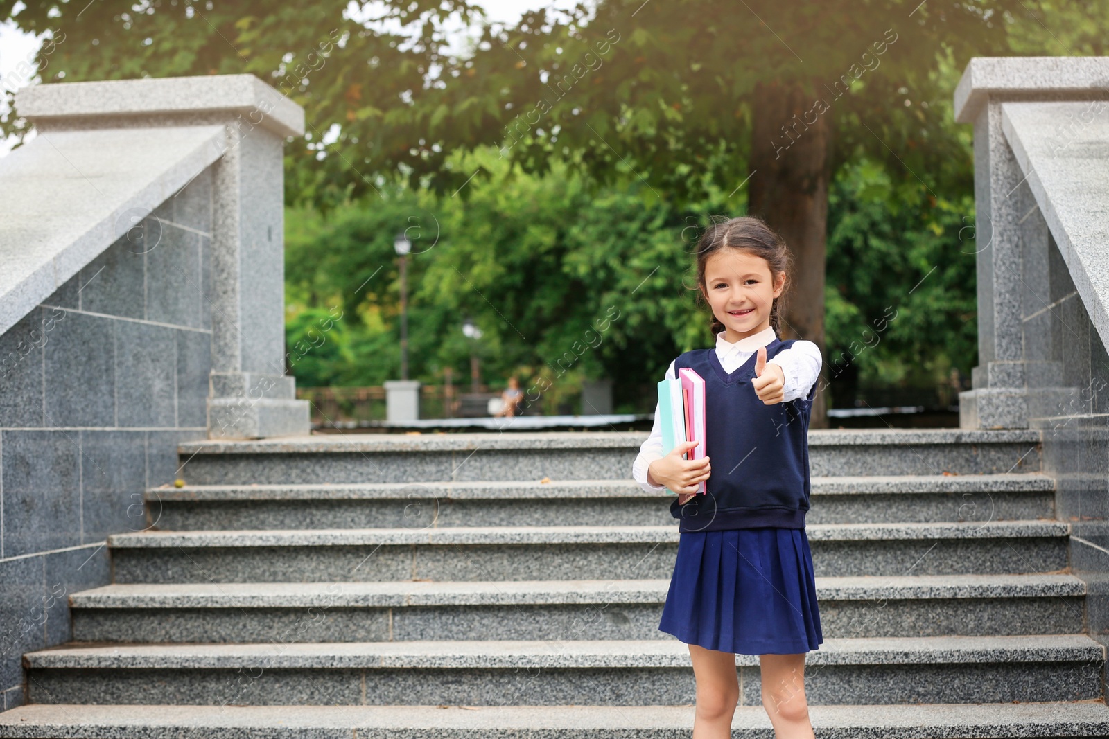 Photo of Cute school child with stationery near stairs in park