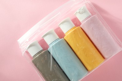 Photo of Cosmetic travel kit in plastic bag on pink background, top view