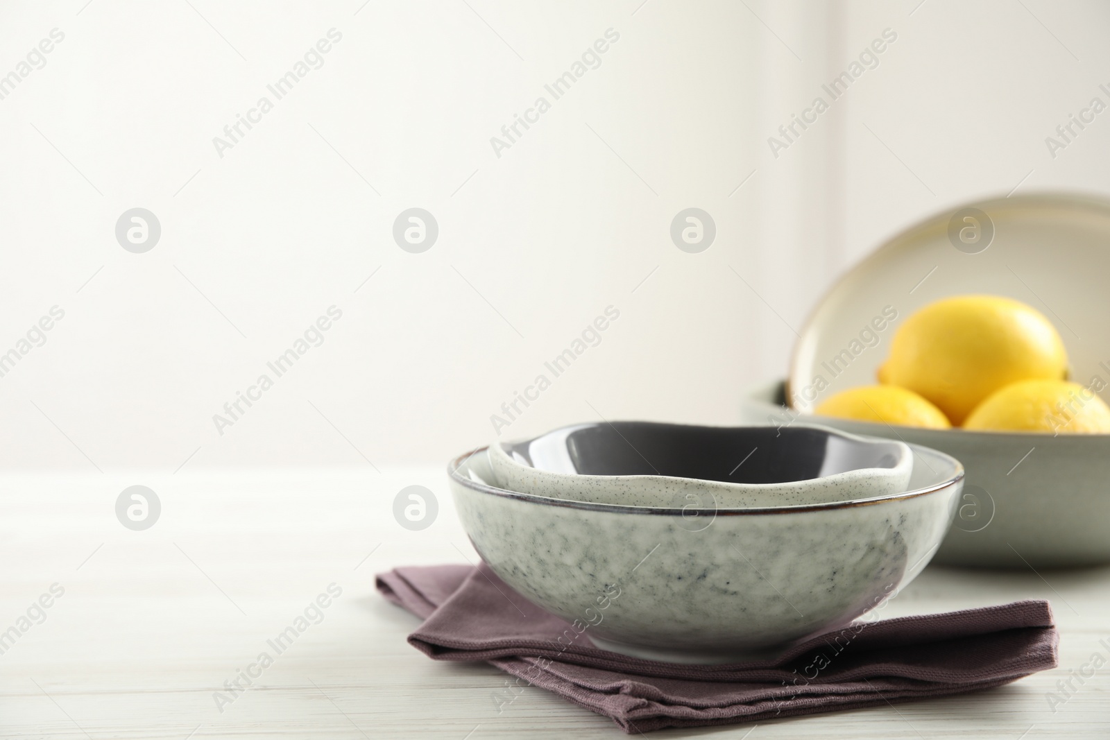 Photo of Set of clean dishware and lemons on white wooden table. Space for text