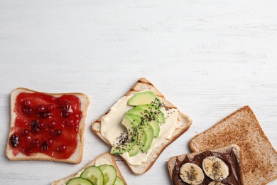 Photo of Slices of bread with different toppings on white wooden table, flat lay