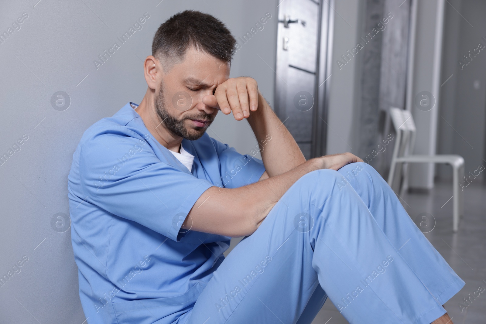 Photo of Exhausted doctor near grey wall in hospital corridor