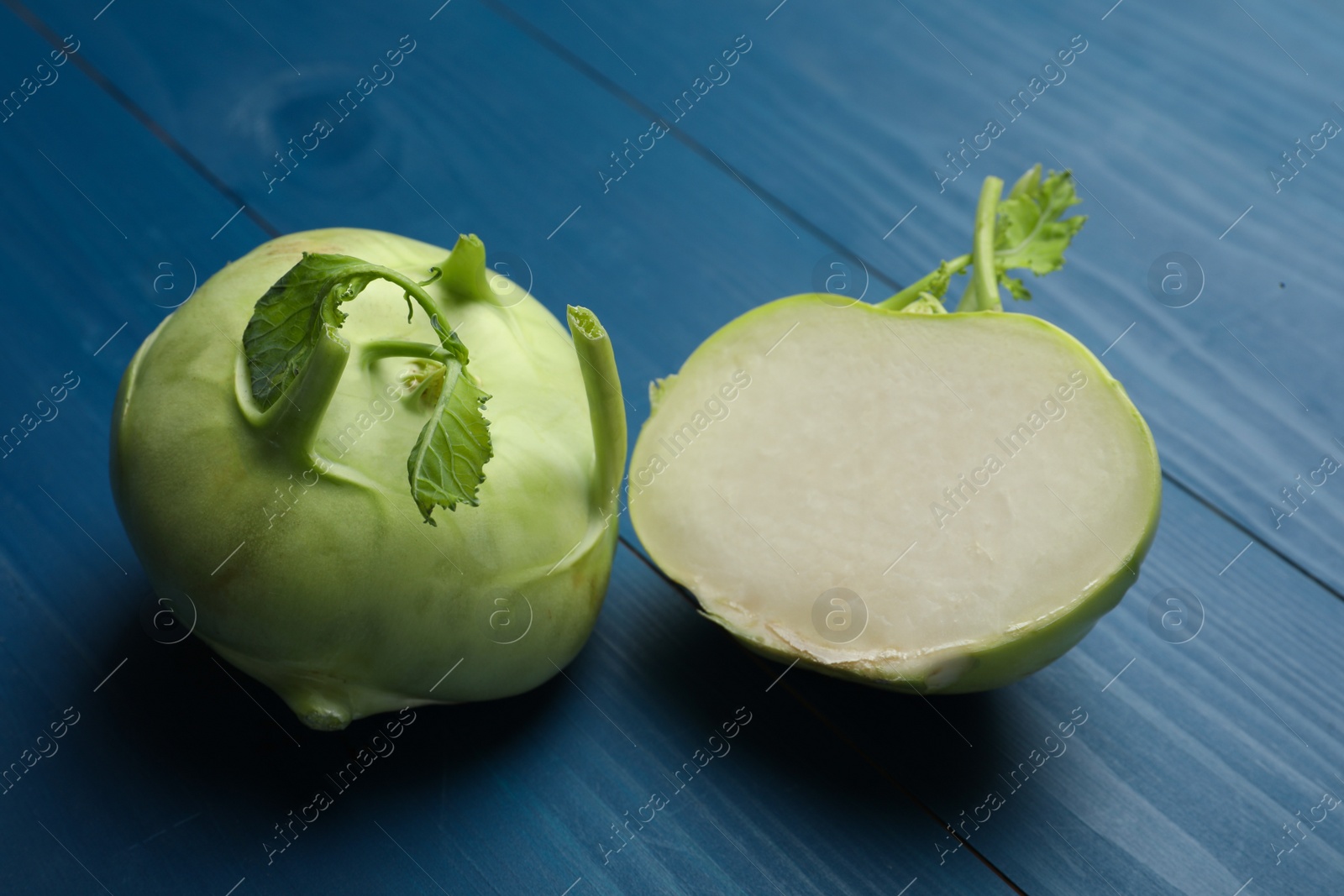 Photo of Whole and cut kohlrabi plants on blue wooden table