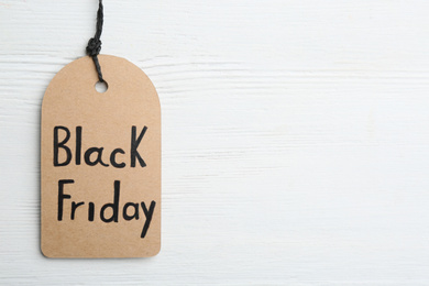 Top view of tag with words BLACK FRIDAY on white wooden background. Space for text