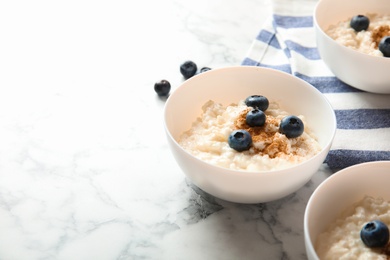 Photo of Creamy rice pudding with cinnamon and blueberries in bowls on marble table. Space for text