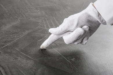 Photo of Person in white glove checking cleanliness of grey stone table, closeup