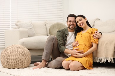 Portrait of happy pregnant woman with her husband on soft carpet at home