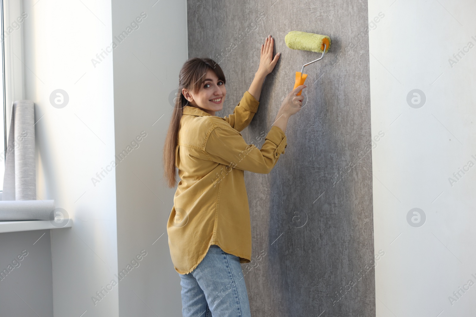 Photo of Woman hanging stylish gray wallpaper in room