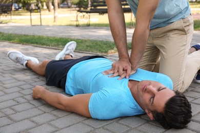 Passerby performing CPR on unconscious man outdoors. First aid