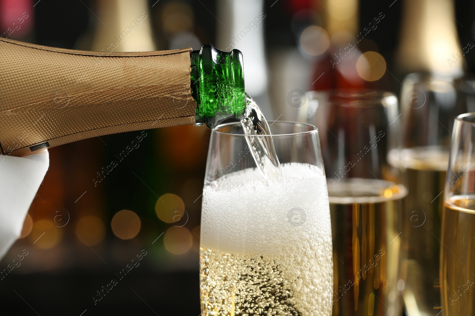 Photo of Pouring champagne into glass on blurred background, closeup