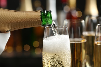 Pouring champagne into glass on blurred background, closeup