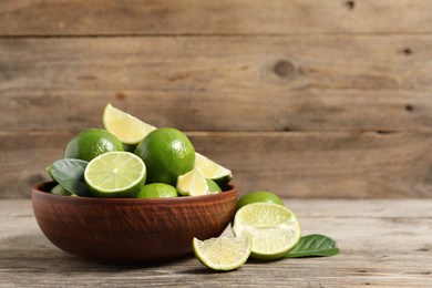 Tasty ripe limes in bowl on wooden table, space for text