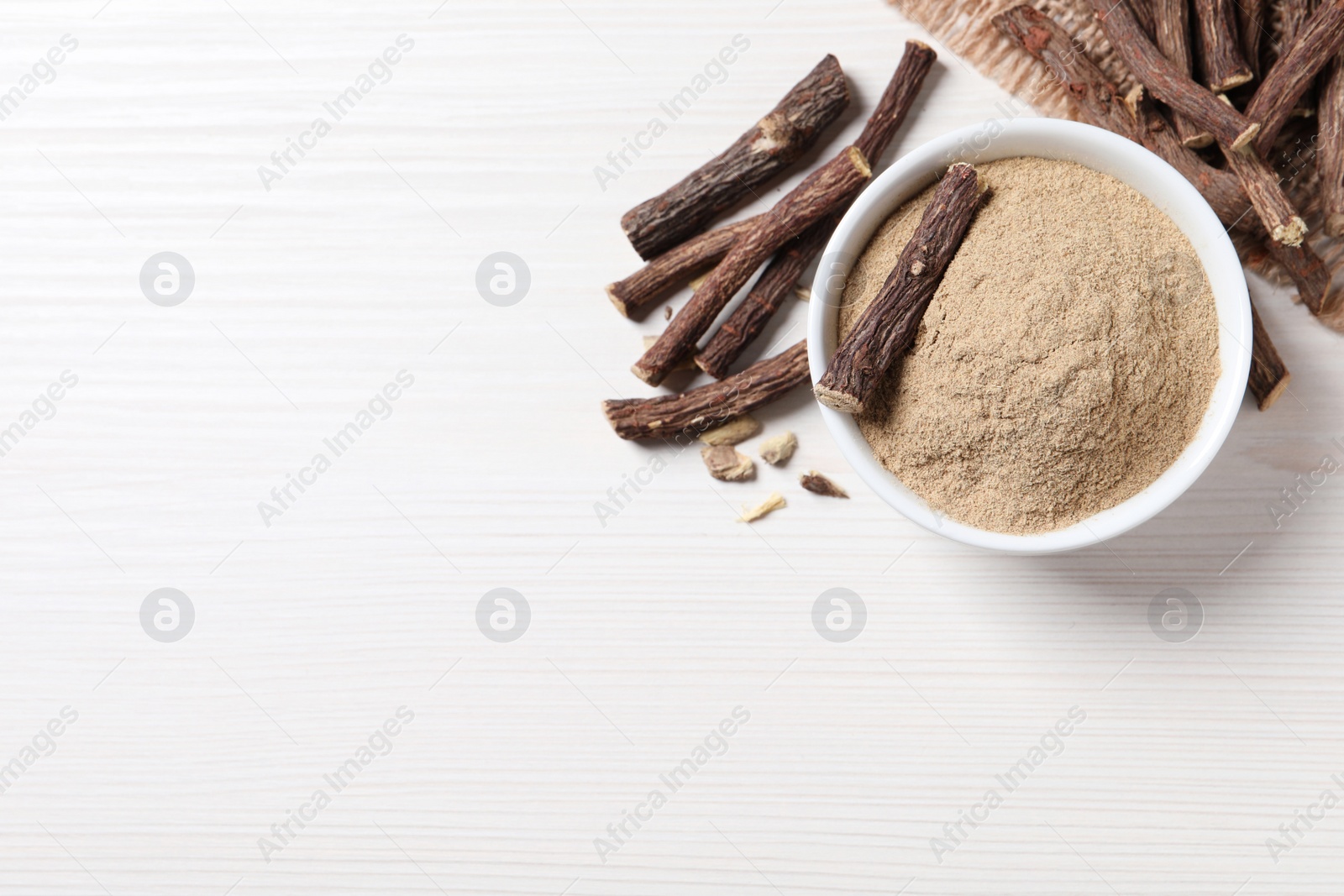Photo of Powder in bowl and dried sticks of liquorice root on white table, flat lay. Space for text