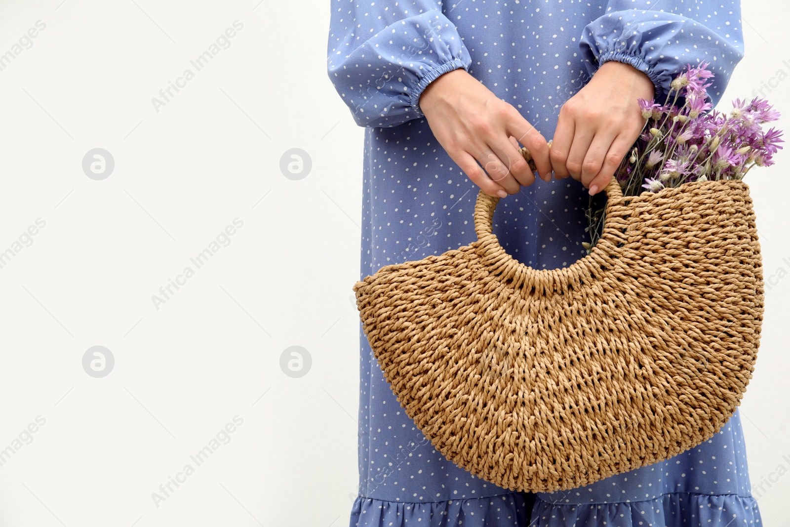 Photo of Woman holding beach bag with beautiful bouquet of wildflowers on white background, closeup