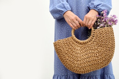 Photo of Woman holding beach bag with beautiful bouquet of wildflowers on white background, closeup