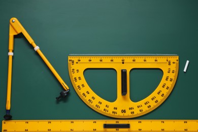 Photo of Protractor, compass, chalk and ruler on green chalkboard, flat lay