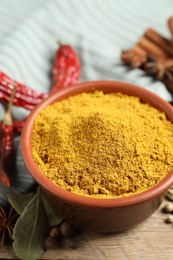 Curry powder in bowl and other spices on wooden table, closeup