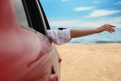 Photo of Woman waving from car on beach, closeup. Summer vacation trip