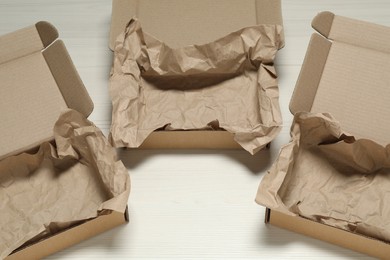 Photo of Open cardboard boxes with crumpled paper on white wooden floor, above view