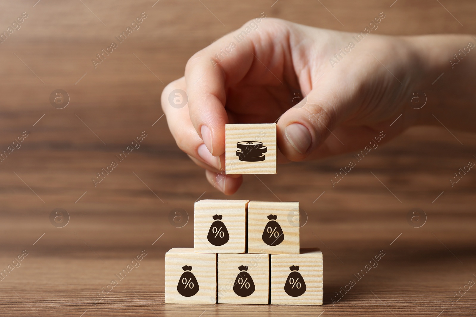 Image of Woman putting cube with illustration of coins on other ones with percent signs on wooden table, closeup