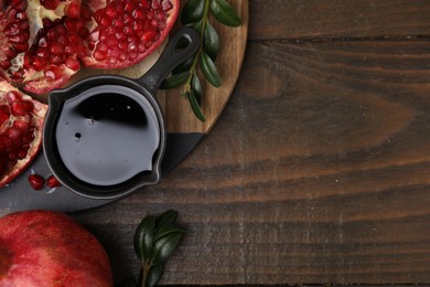 Photo of Tasty pomegranate sauce, fruits and branches on wooden table, top view. Space for text